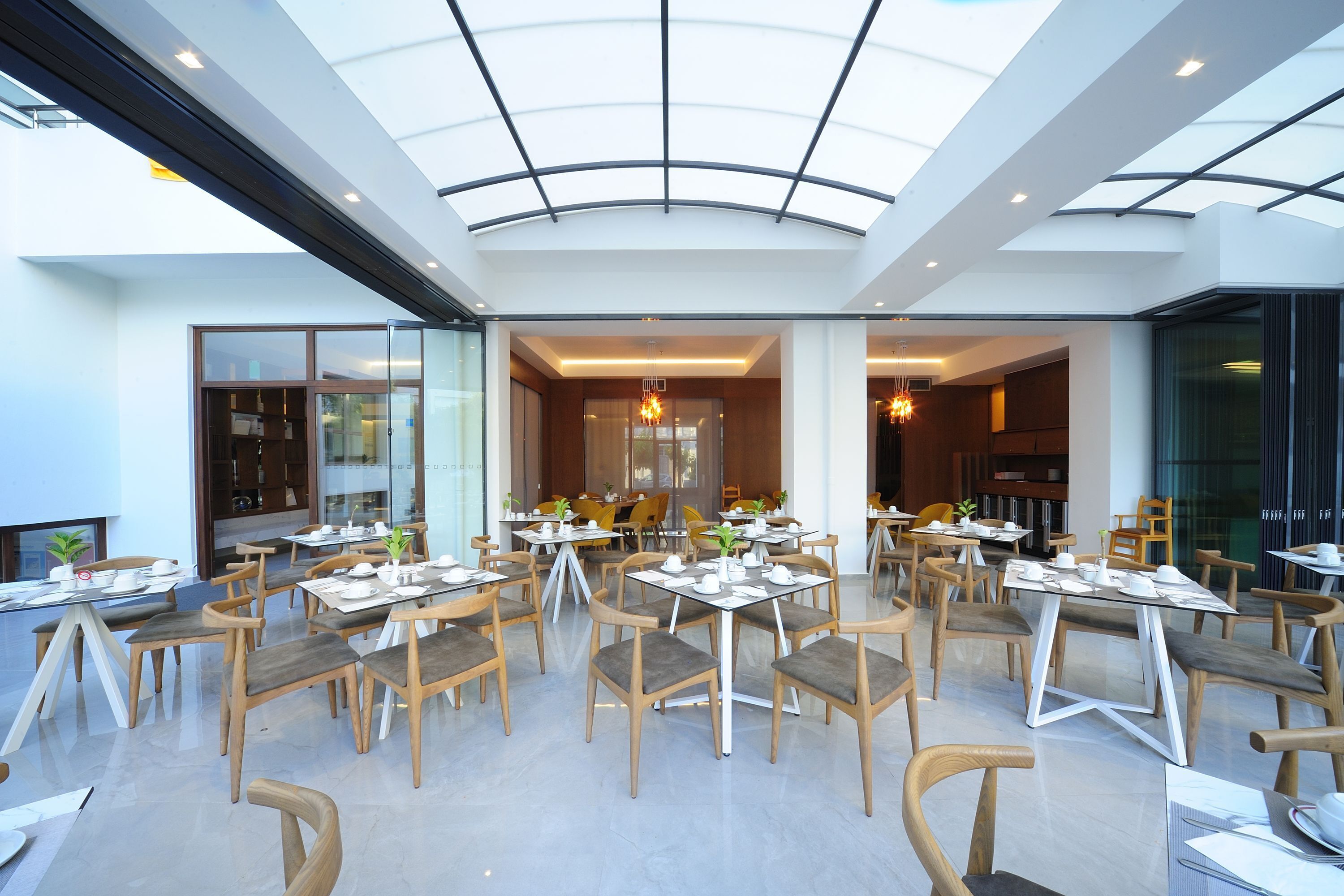 A spacious dining area with multiple tables and chairs, a glass ceiling, and a modern interior design.