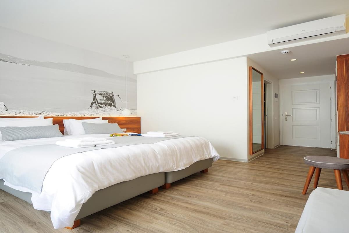 Moderni hotellihuone, jossa on suuri sänky, puinen pääty, pieni oleskelualue ja näkymä rannalle.