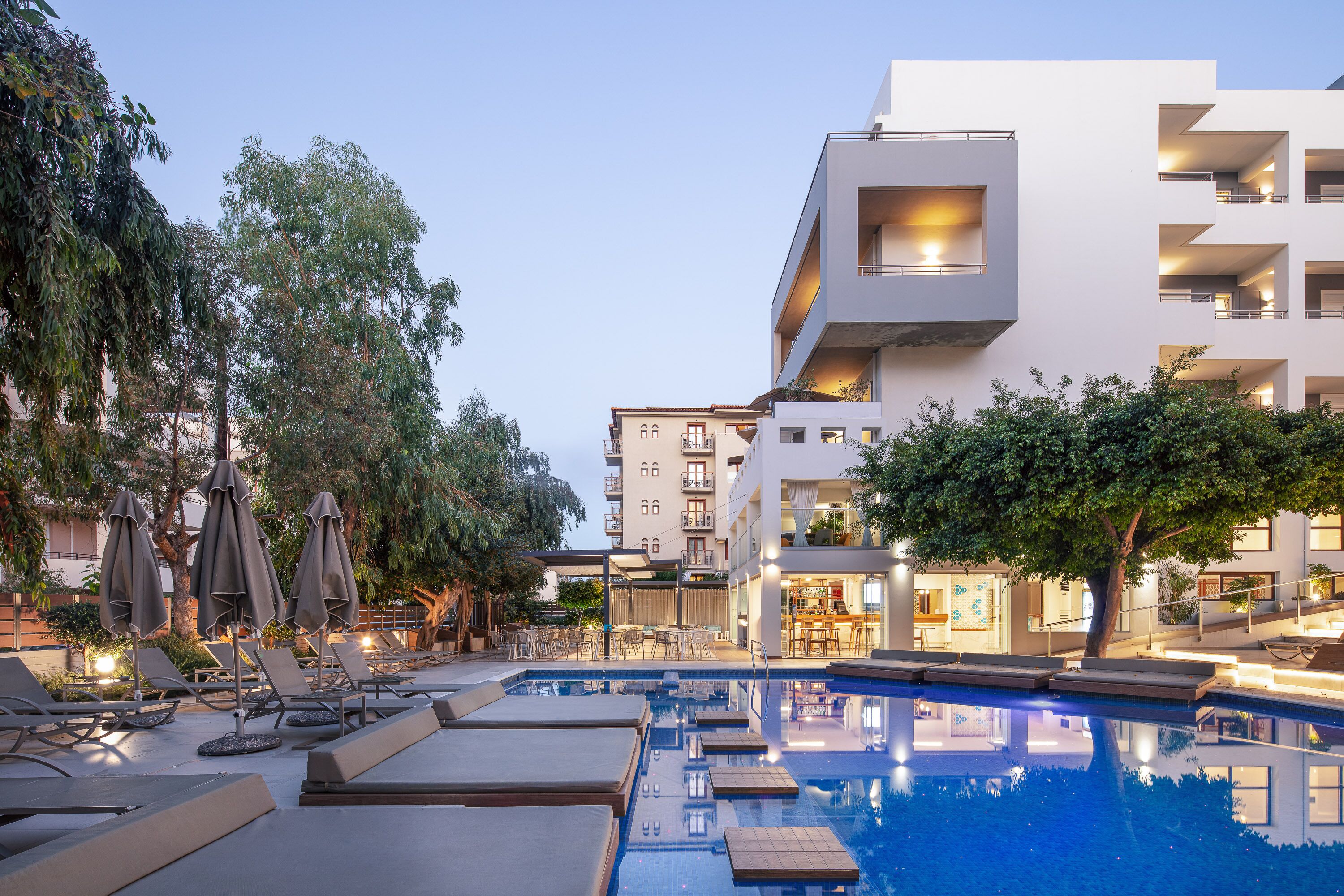 A modern hotel with a swimming pool, lounge chairs, and umbrellas.