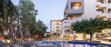 A modern hotel with a swimming pool, lounge chairs, and umbrellas.