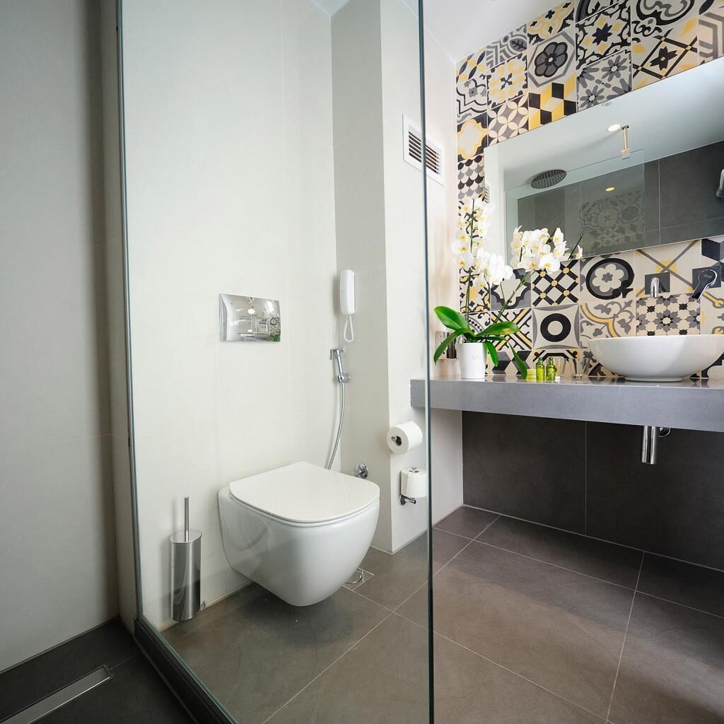A modern bathroom with a white toilet, a glass shower enclosure, and a sink with a decorative tile backsplash.