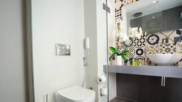 A modern bathroom with a white toilet, a glass shower enclosure, and a sink with a decorative tile backsplash.