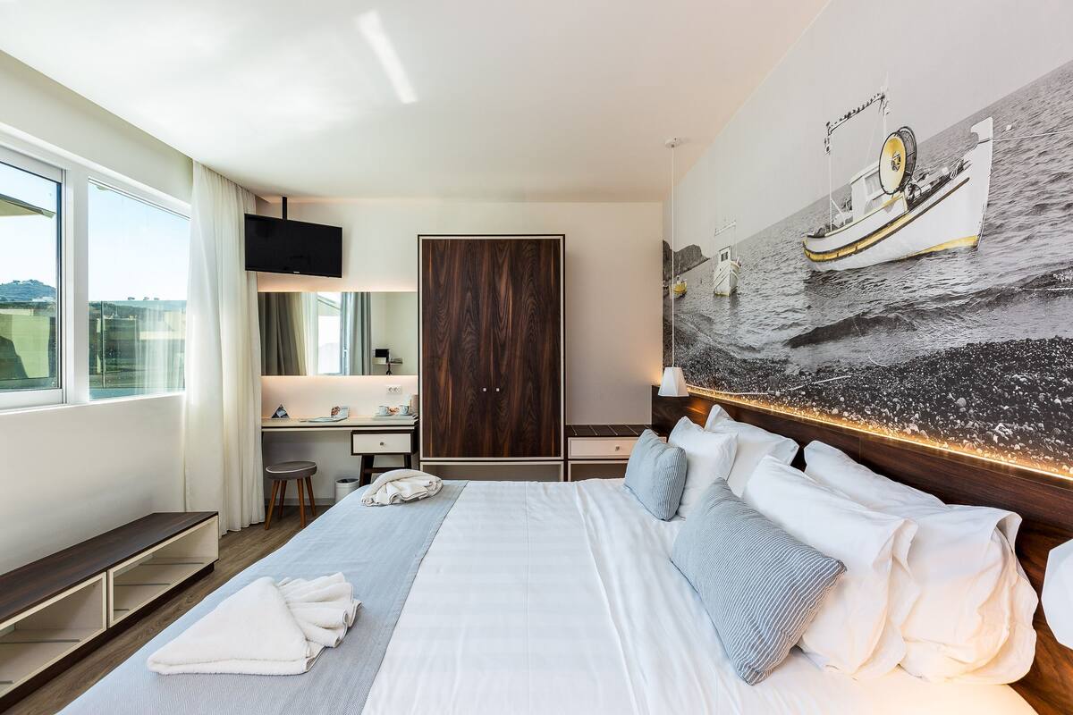 Moderni hotellihuone, jossa on suuri sänky, työpöytä, vaatekaappi ja näkymä merelle.