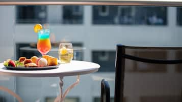 A table with a colorful drink, a glass of juice, and a plate of food on a balcony with a view of buildings.