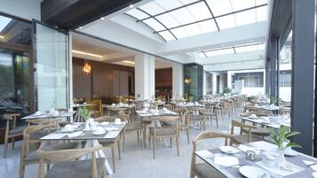 Un vaste espace dédié à la salle à manger, avec de nombreuses tables et chaises, de grandes fenêtres et un aménagement intérieur moderne.