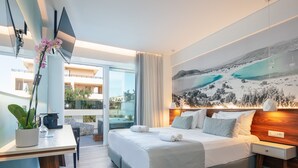 A modern hotel room with a large bed, a desk with a plant, a view of the sea through the balcony, and a painting of a coastal landscape. - Atrium Ambiance Hotel (Rethymno)