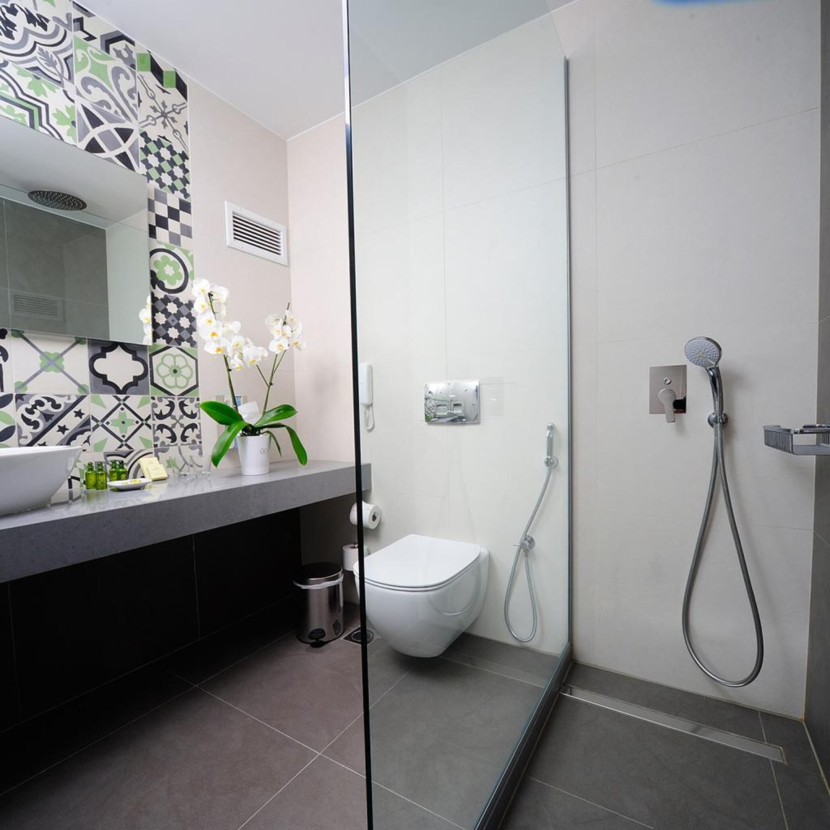A modern bathroom with a glass shower enclosure, a white toilet, and a sink with a patterned backsplash.