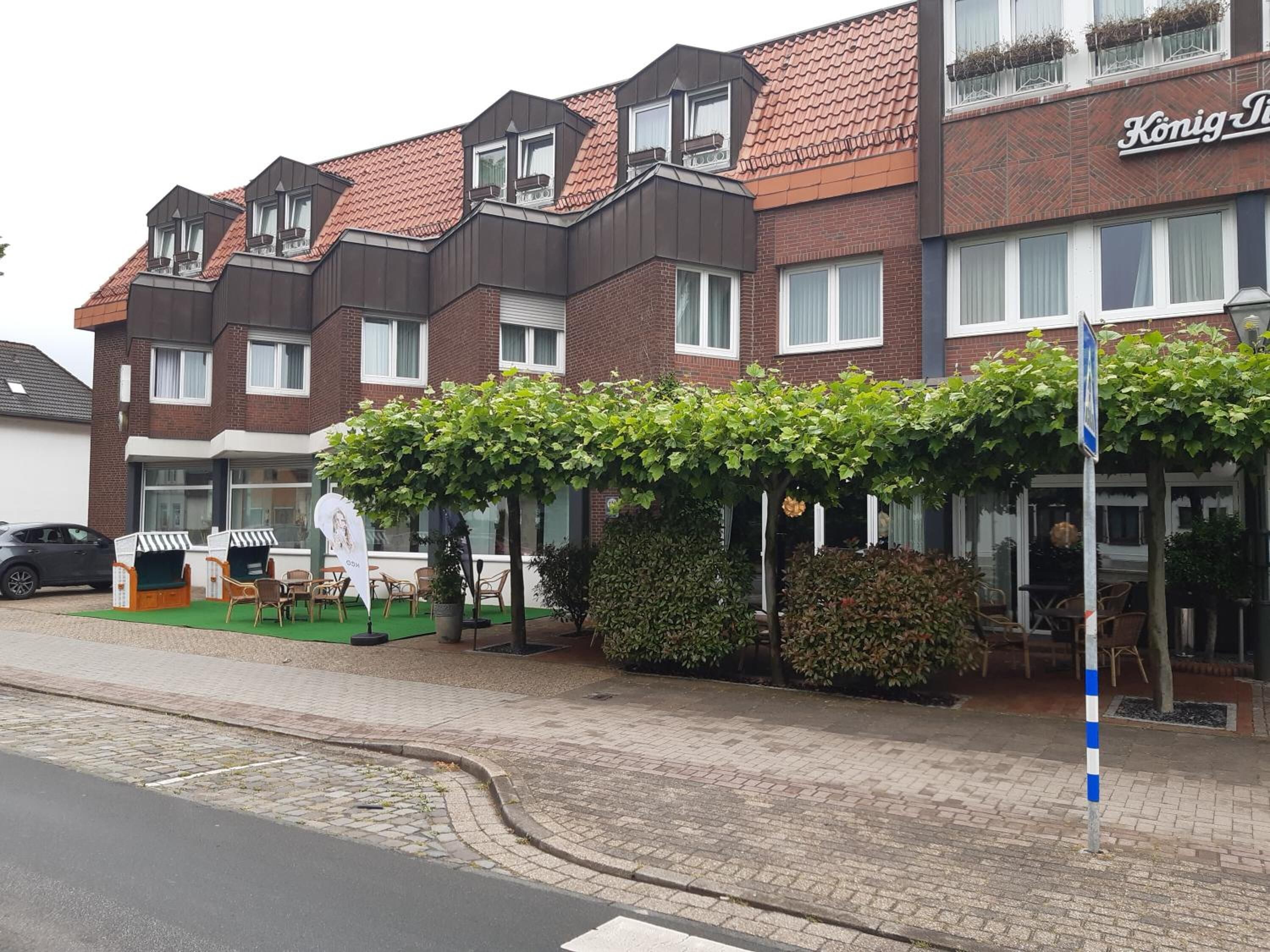Een hotel met een bakstenen gevel, meerdere ramen en een overdekt terras met stoelen en tafels.