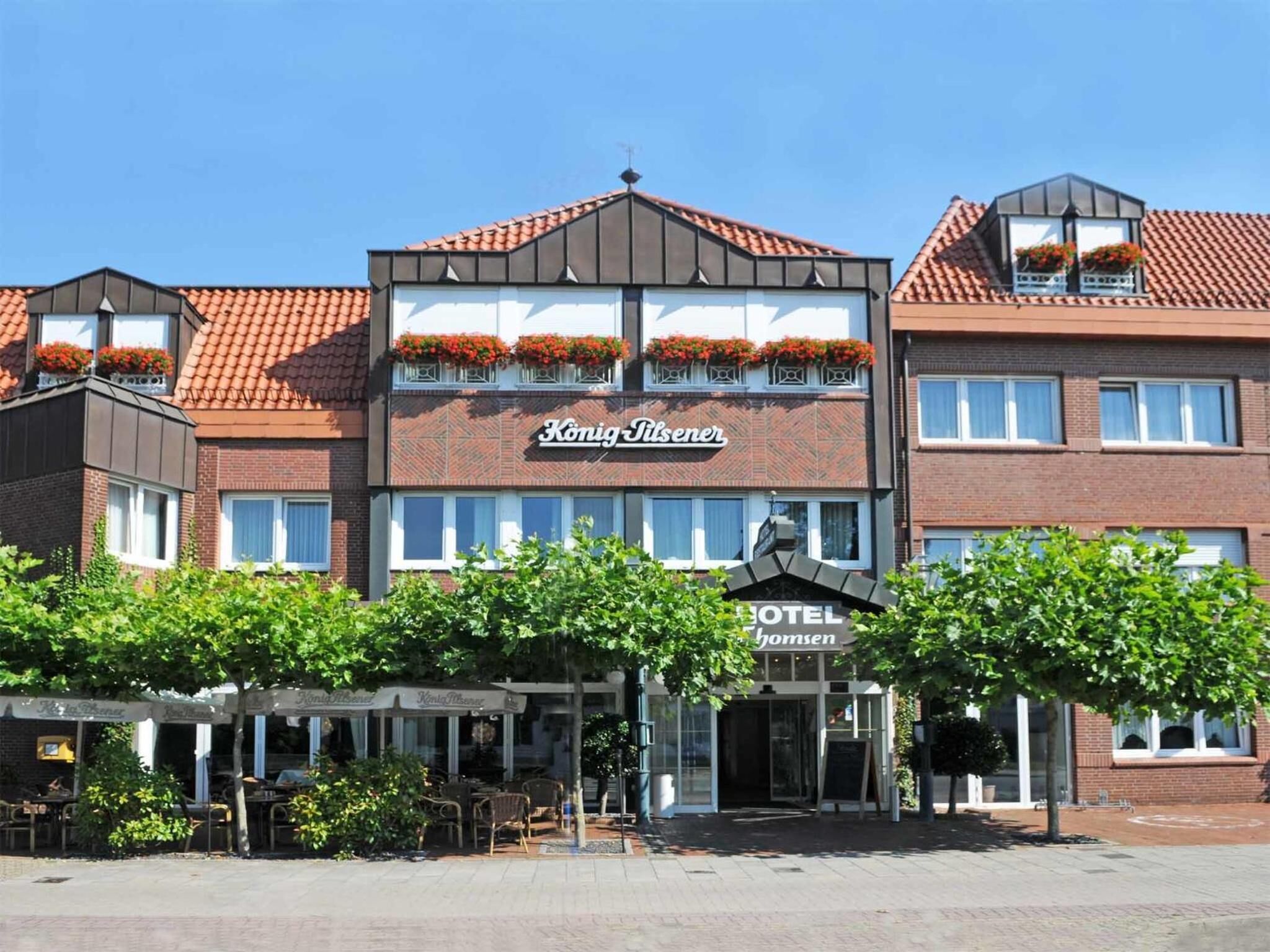 A hotel named "Konig Dilsener" with a modern facade, multiple windows, and flower boxes on the roof.