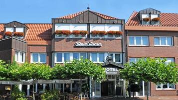 A hotel named "Konig Dilsener" with a modern facade, multiple windows, and flower boxes on the roof.