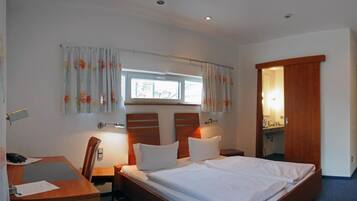 A hotel room with a bed, a desk, a chair, a nightstand, and a bathroom door.