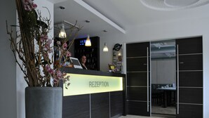 A reception area with a 'RECEPTION' sign, a large potted plant, and a digital clock displaying 11:30. - Hotel-Restaurant Thomsen (Delmenhorst)