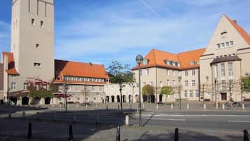 Un bâtiment historique doté d’une tour imposante, d’une cour avec des bancs et d’une rue qui s’étend devant lui.