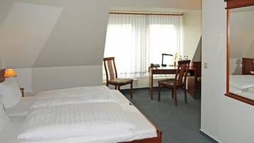 A hotel room with two beds, a desk, a chair, and a large mirror.
