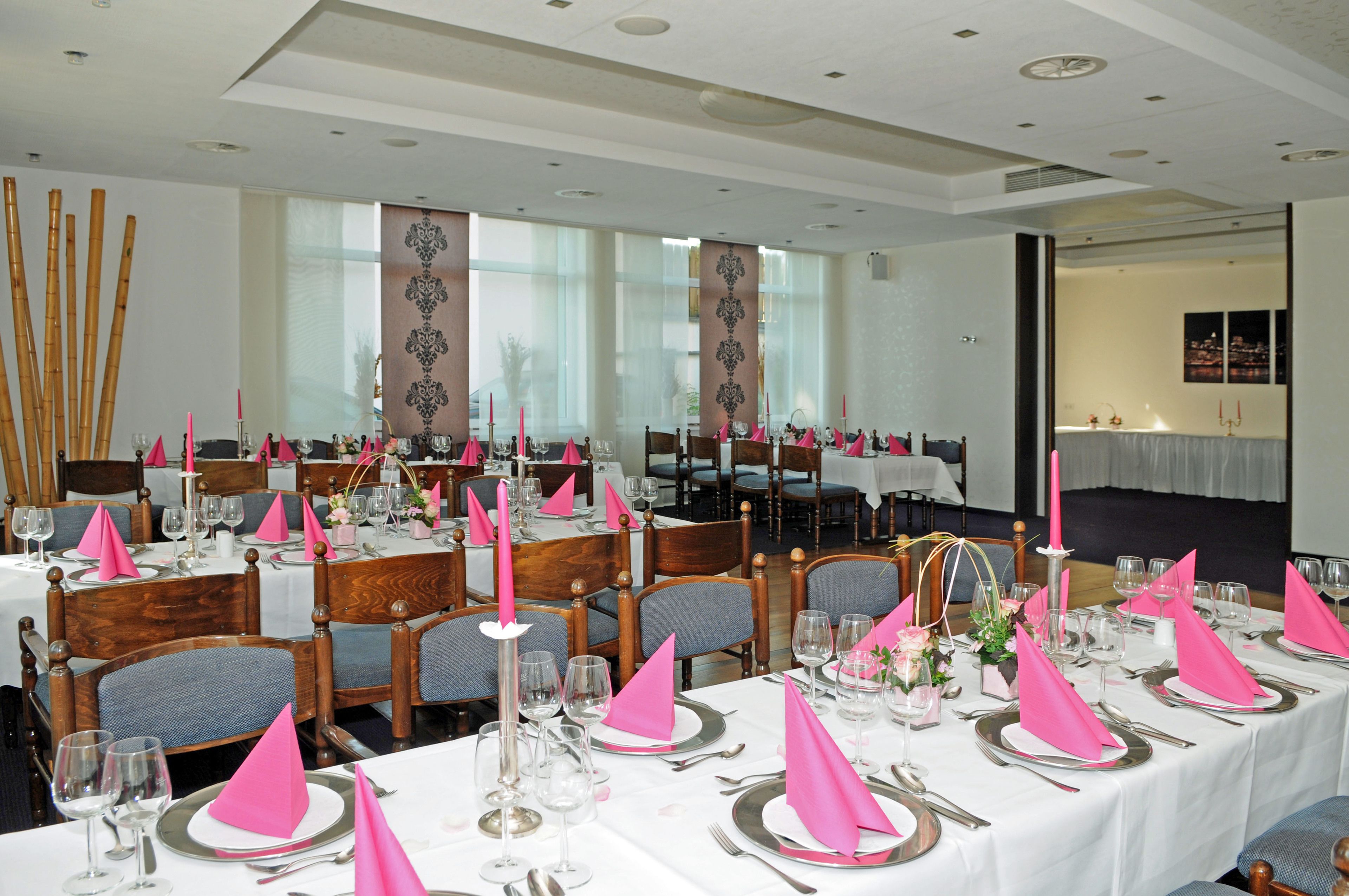 A banquet hall with tables set for a formal event, featuring white tablecloths, pink napkins, and silverware.