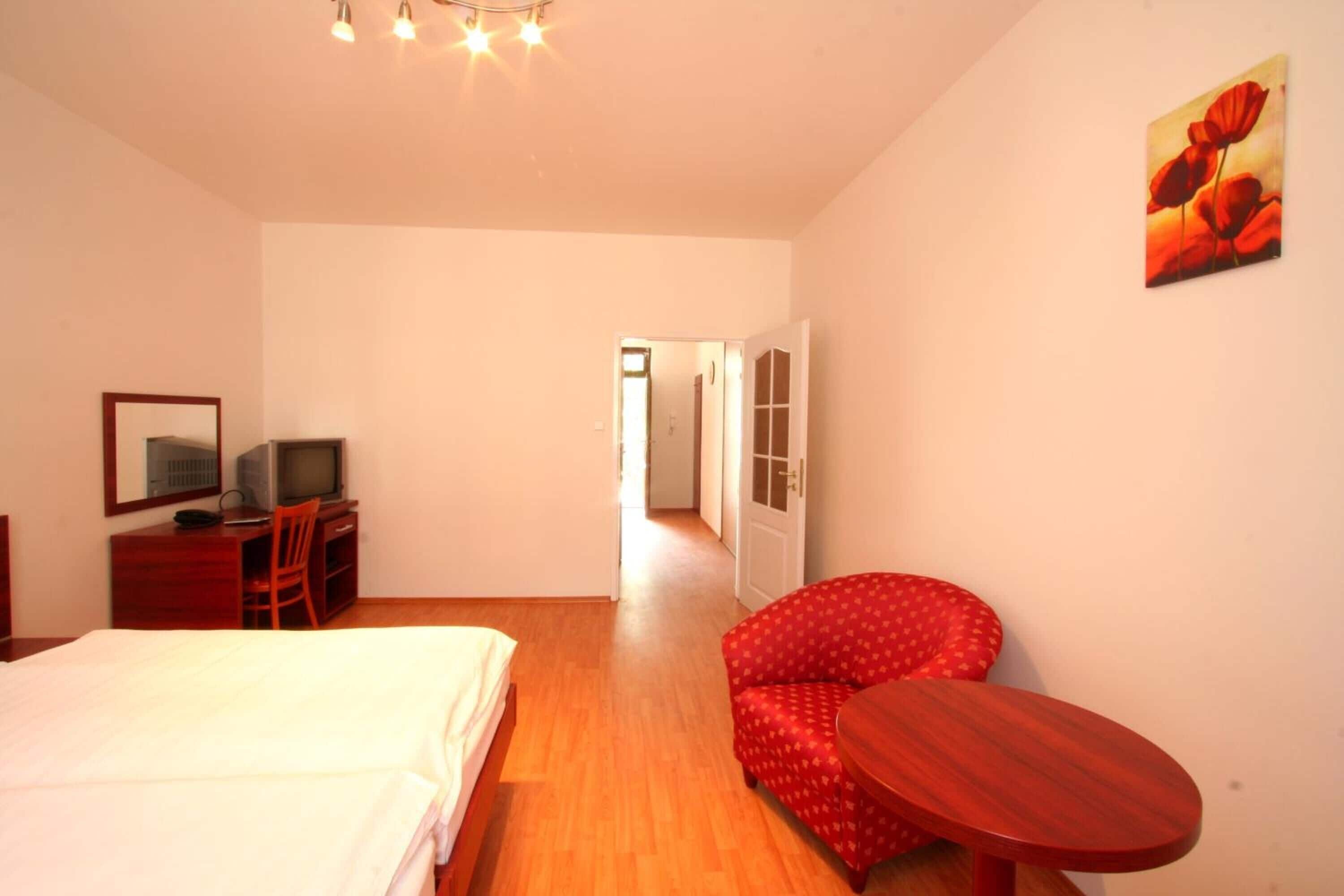 A hotel room with a bed, a desk with a computer, a chair, a small table, and a painting on the wall.
