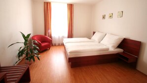 A bedroom with a wooden floor, a bed with white bedding, a red chair, a potted plant, and a window with curtains. - Aparthotel Susa (Prague)