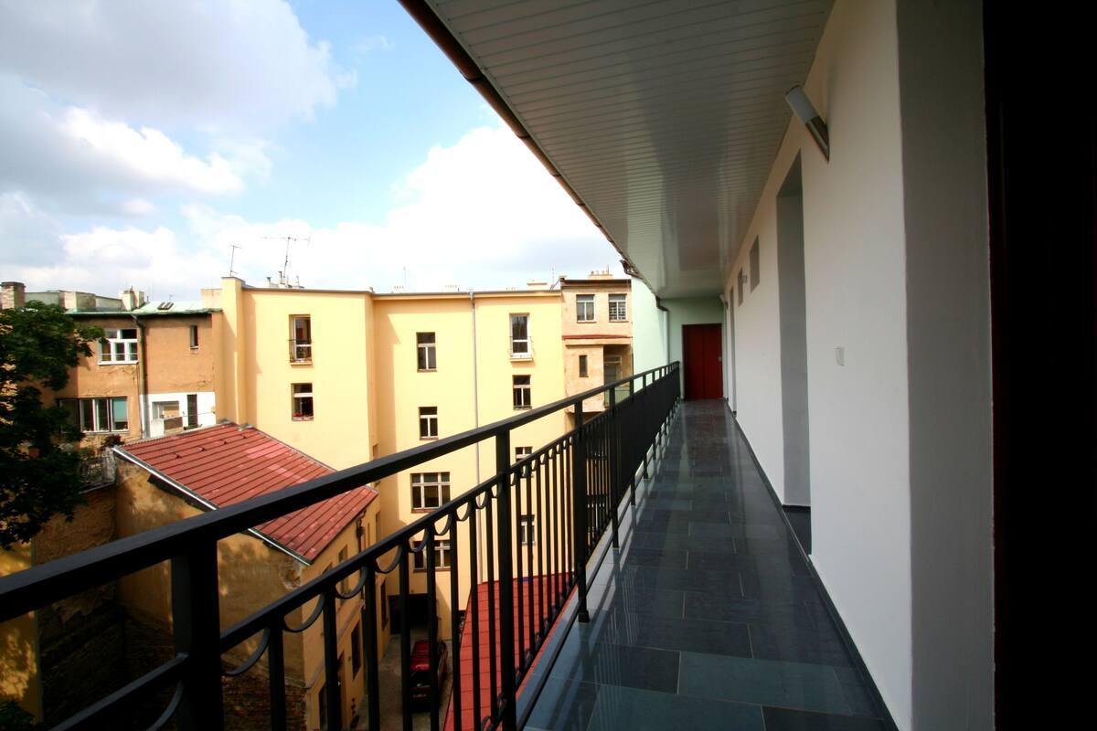 A balcony with a view of adjacent buildings and a red car parked below.