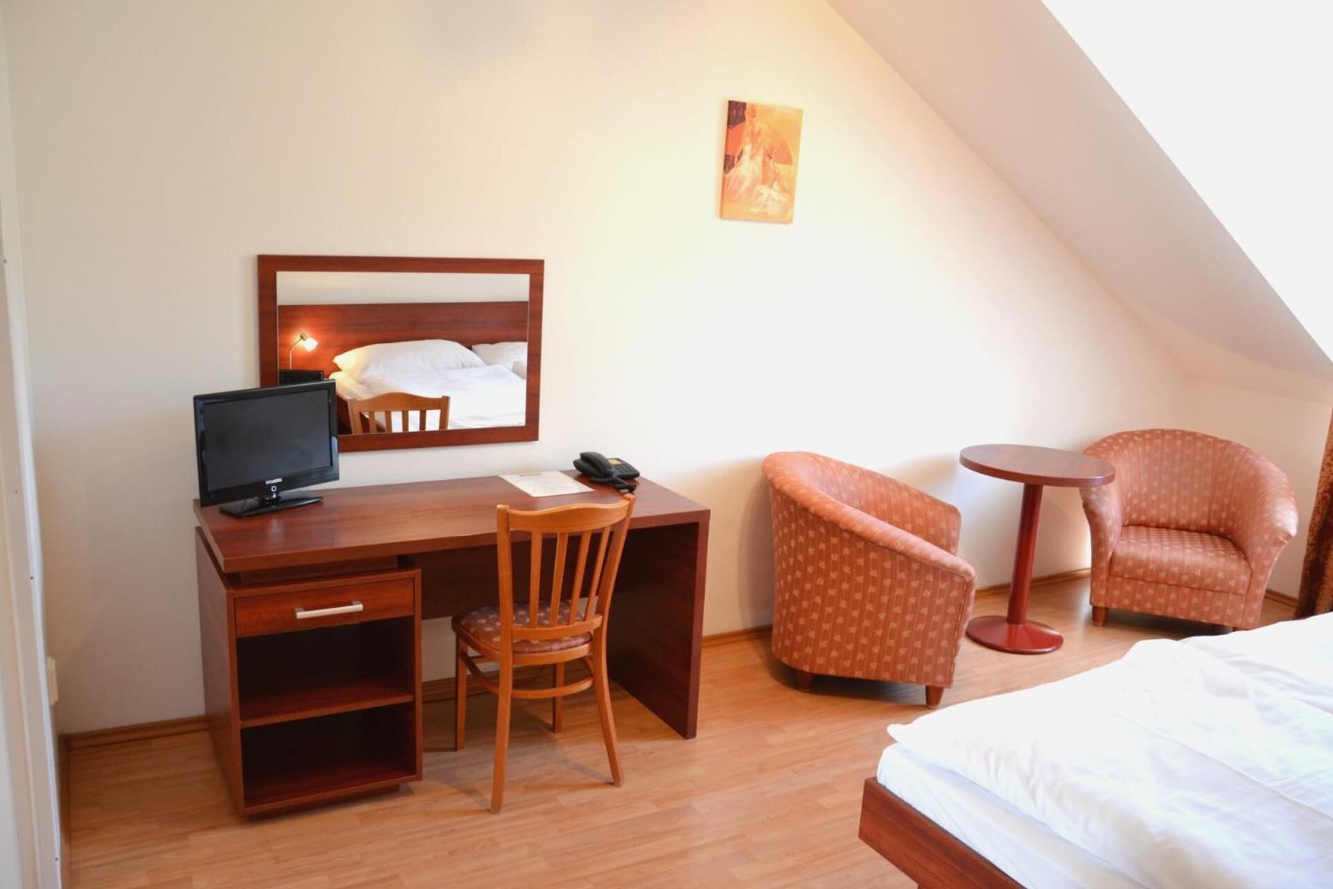 A hotel room with a wooden desk, a computer, a chair, a small round table, and a bed.