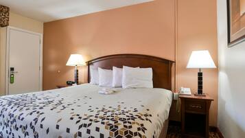 A hotel room with a large bed, two bedside lamps, a nightstand with a phone, and a door with a green sign.