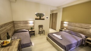 Habitació d'hotel amb dos llits, una taula petita amb una cistella de fruita, una cadira i una nitzeta amb una làmpada.