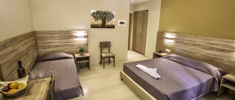 A hotel room with two beds, a small table with a basket of fruit, a chair, and a nightstand with a lamp.