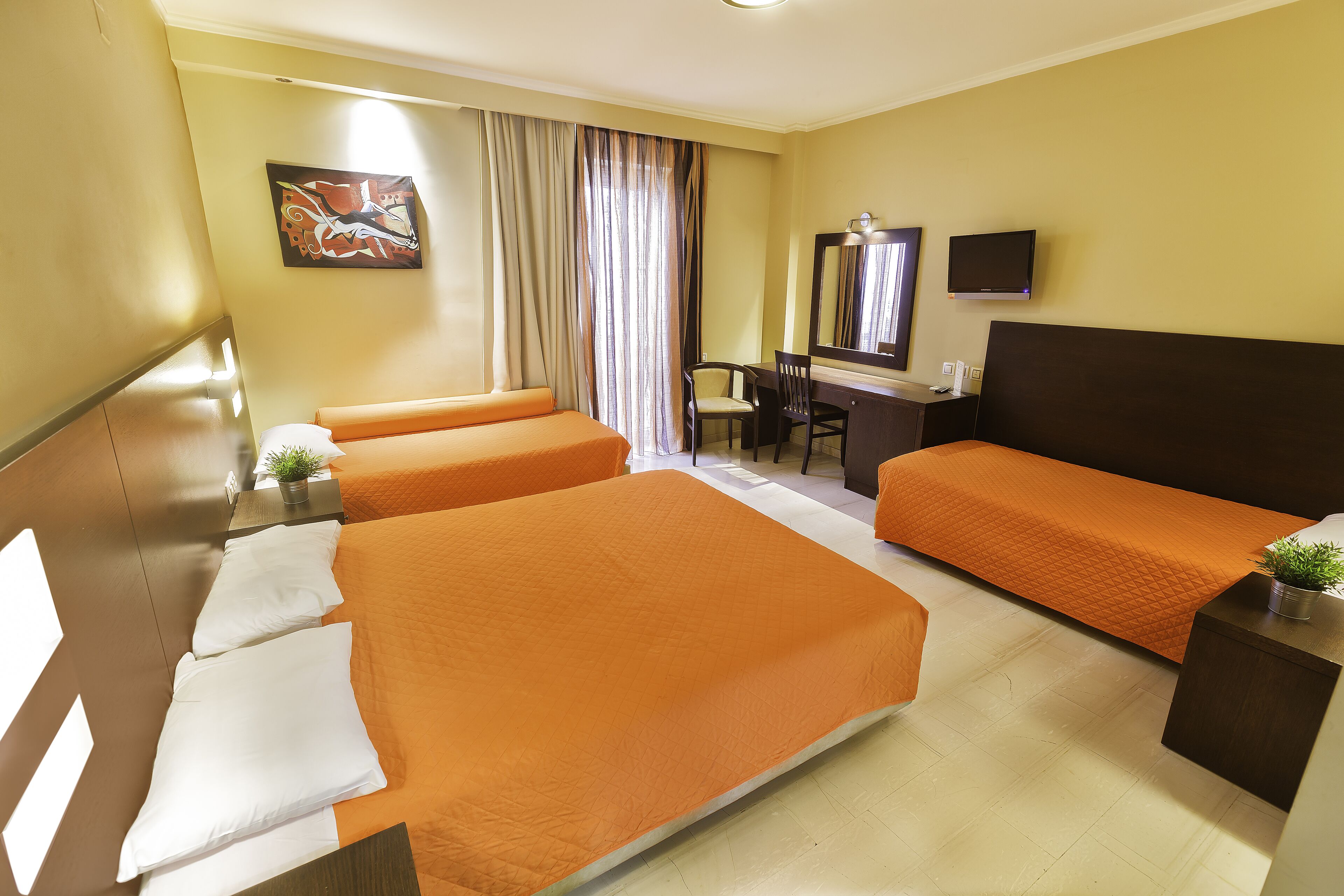 Habitación de hotel con tres camas, un escritorio, una silla, un televisor y un cuadro en la pared.