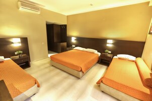 Quarto de hotel com uma cama grande, duas mesas de cabeceira, um criado-mudo, um espelho e ar condicionado fixado na parede.