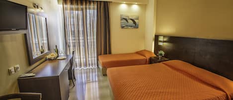 A hotel room with a bed, a desk with a mirror, a television, and a window with curtains.
