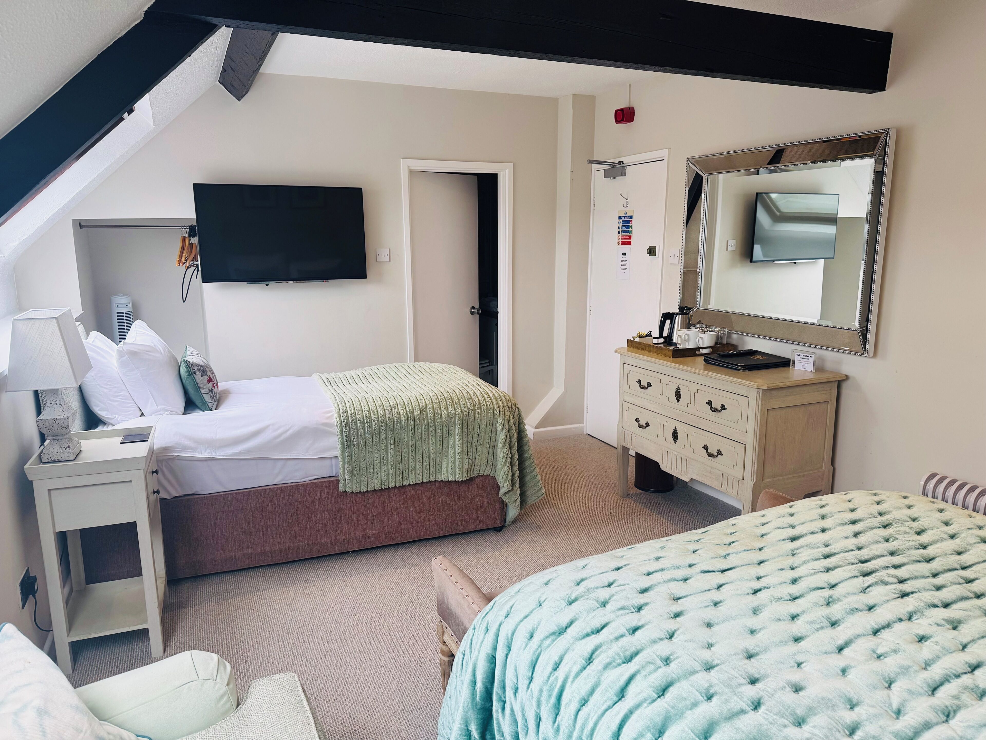 Une chambre à coucher comprenant un lit, une table de chevet, une commode, un miroir et un téléviseur fixé au mur.
