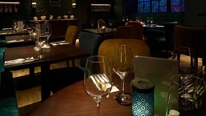 L’intérieur d’un restaurant à la lumière tamisée, avec des tables dressées pour le dîner, un lustre et un meuble à bouteilles de vin accroché au mur.