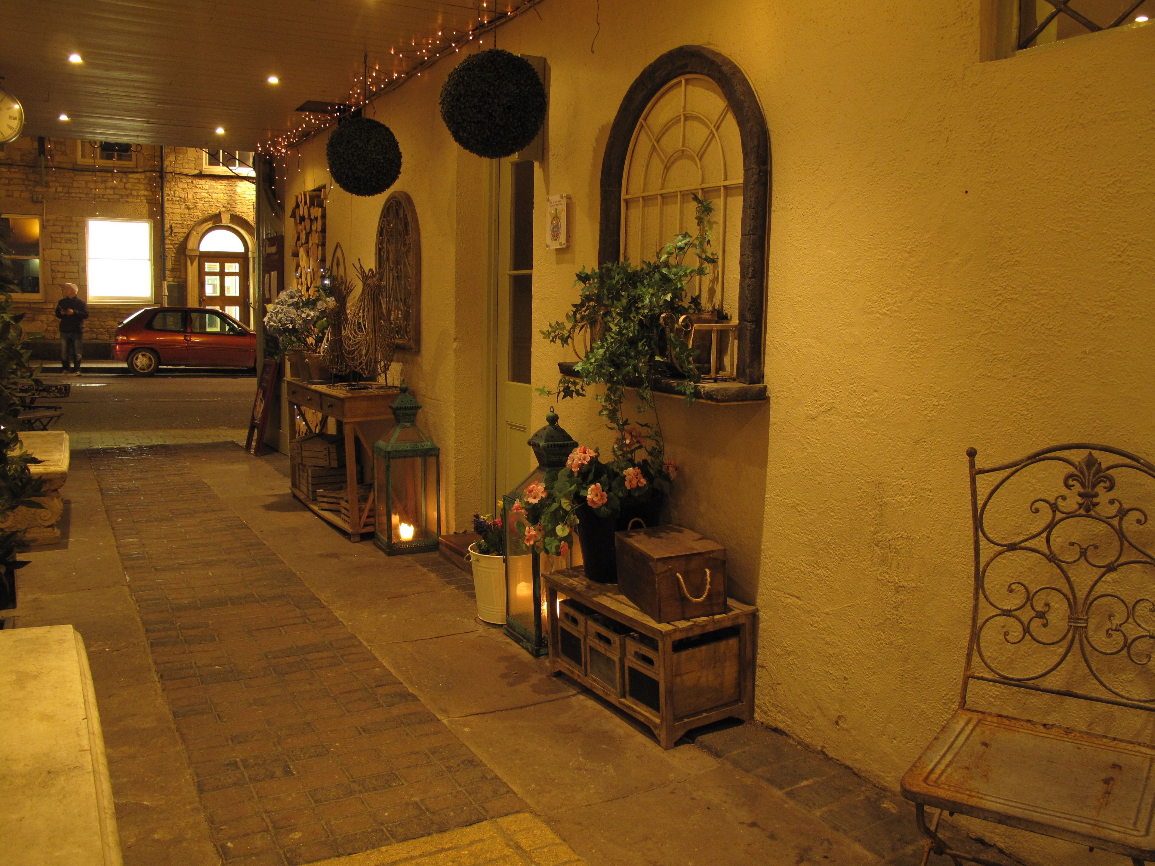 A warmly lit corridor with a vintage car parked outside, a bench, and decorative lanterns.