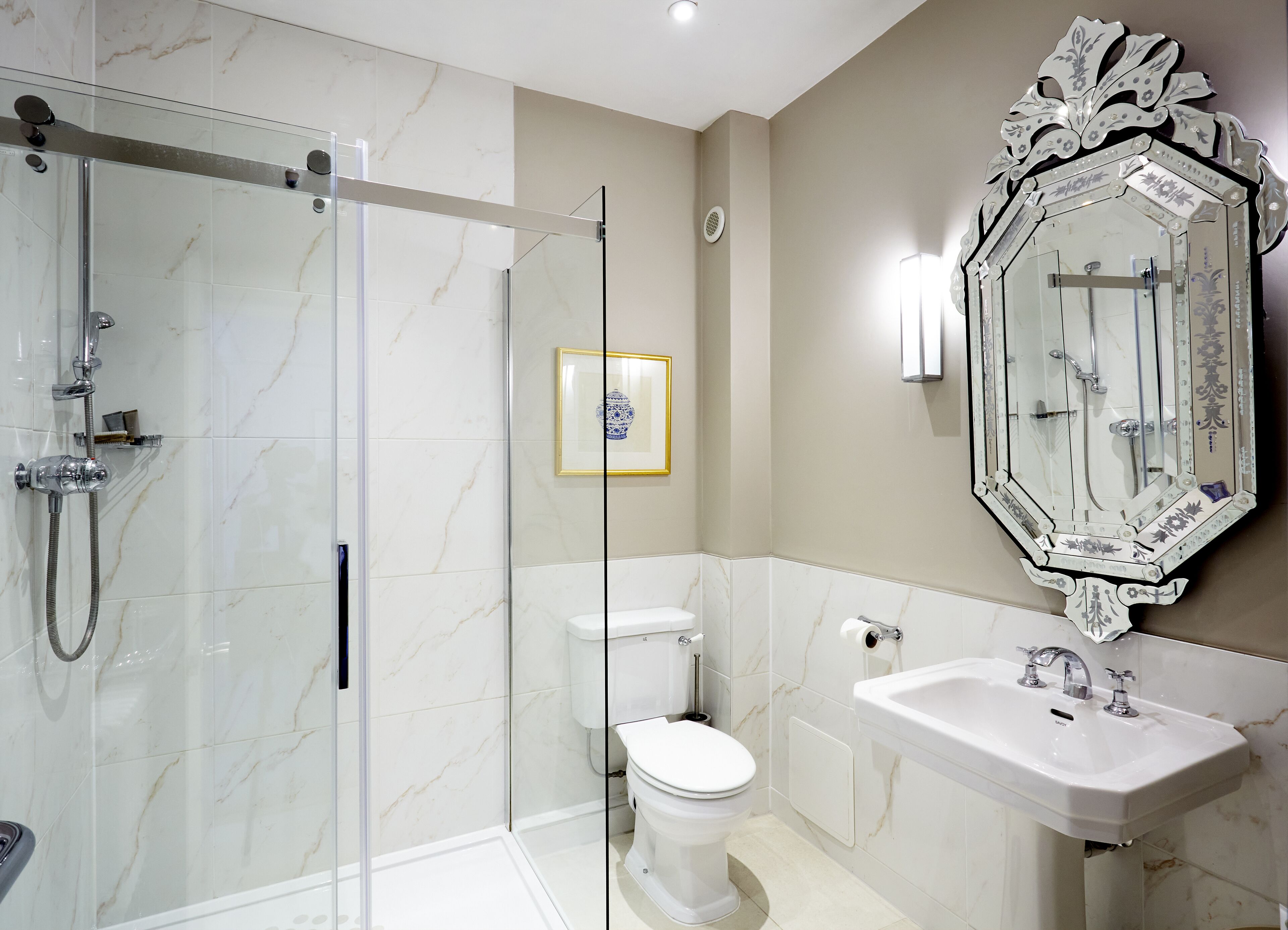 Un baño moderno con ducha envuelta en vidrio, inodoro, lavamanos y un espejo decorativo.