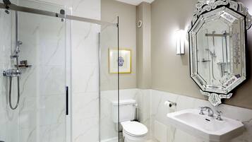 Un baño moderno con ducha envuelta en vidrio, inodoro, lavamanos y un espejo decorativo.