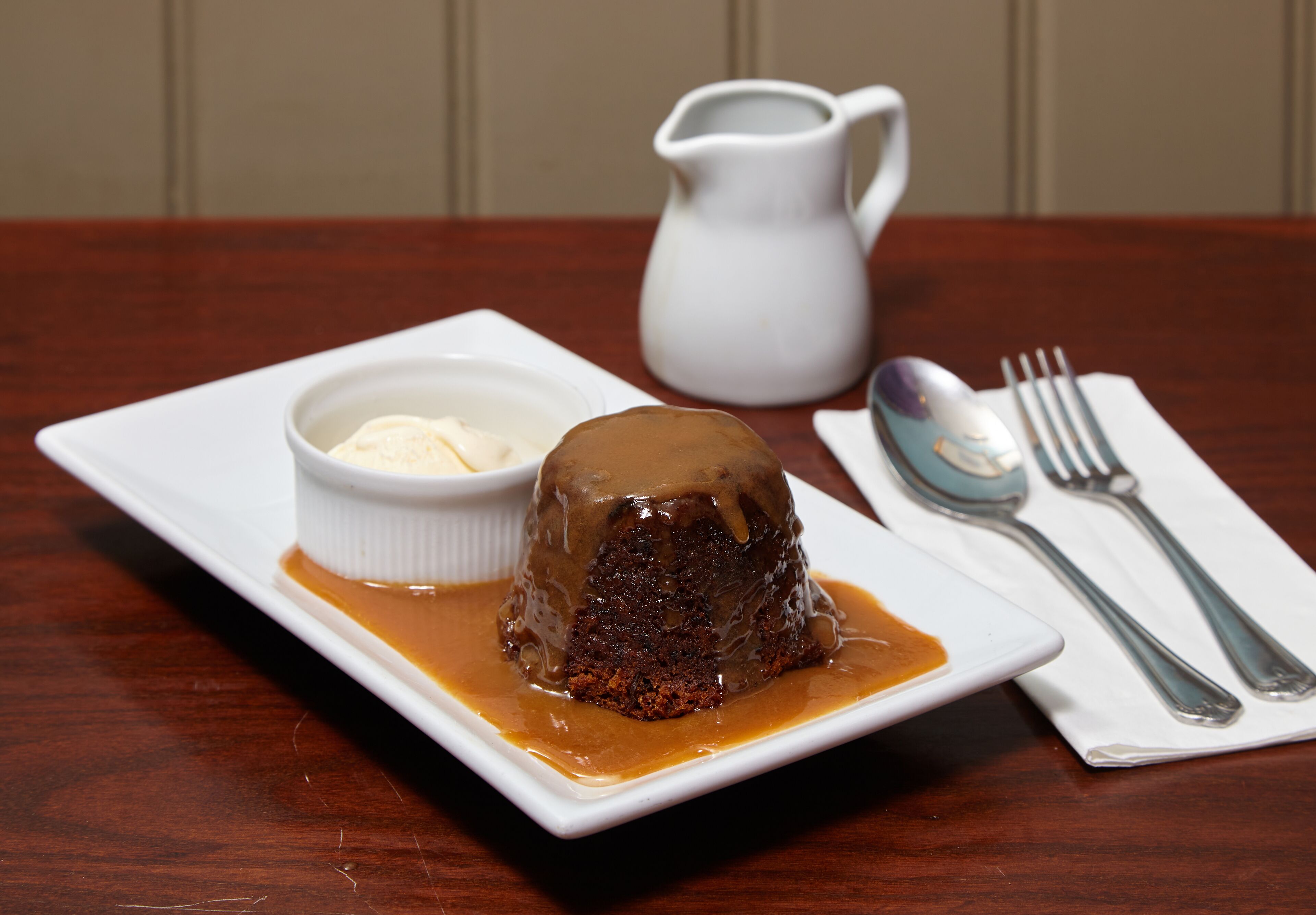 Un plato de postre con un pudin de caramelo pegajoso y un pequeño recipiente de helado.