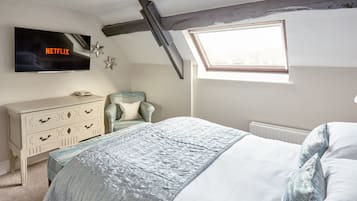 Un dormitorio con cama, cómoda, silla, televisor montado en la pared y tragaluz.