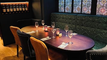 Un restaurante con una mesa redonda, sillas, botellas de vino en estantes y ventanas con diseños.