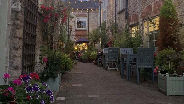 Une ruelle étroite bordée de bâtiments en pierre, illuminée de guirlandes lumineuses et agrémentée de plantes en pot.