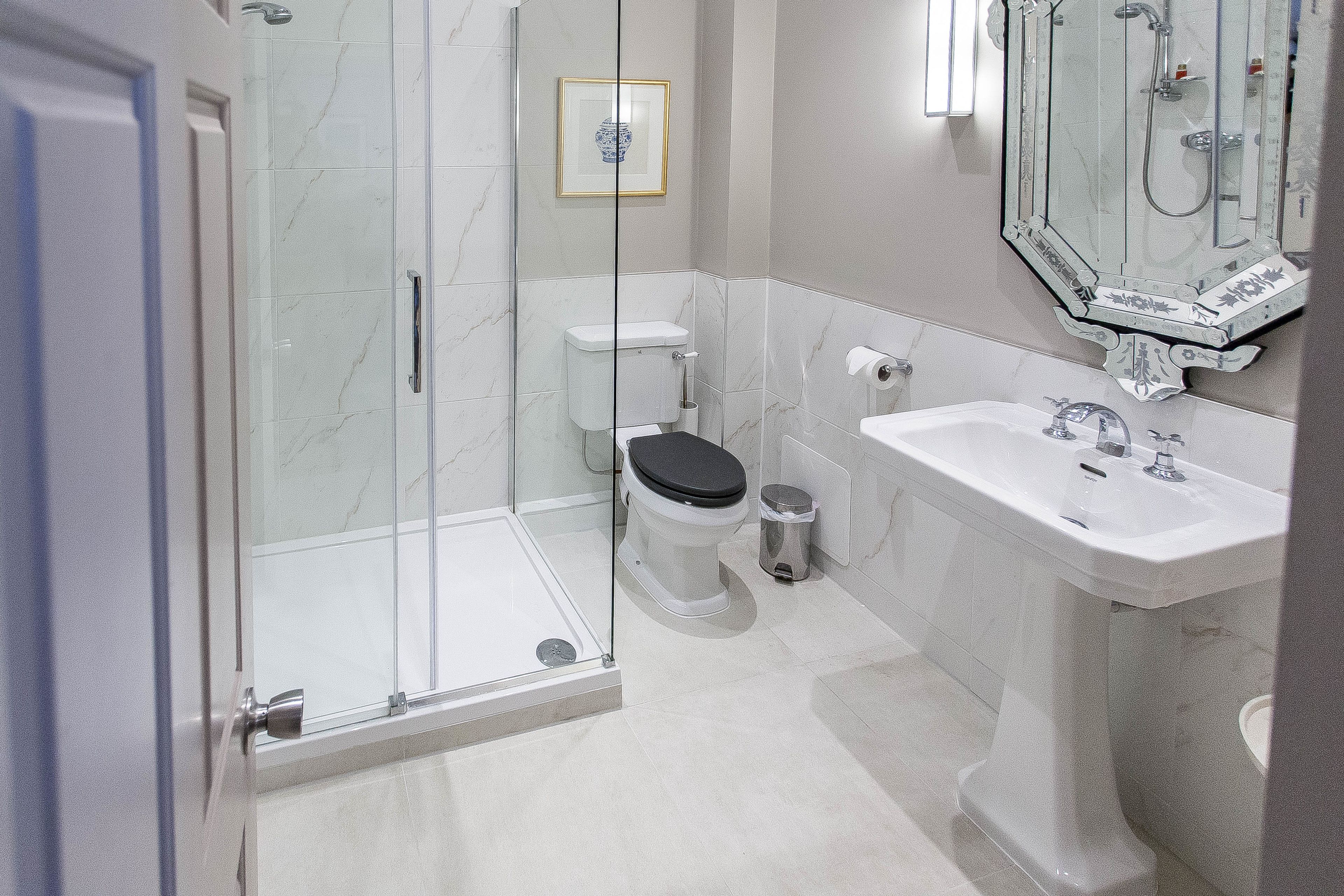 Un baño moderno con ducha envuelta en vidrio, inodoro y lavamanos sobre pedestal.