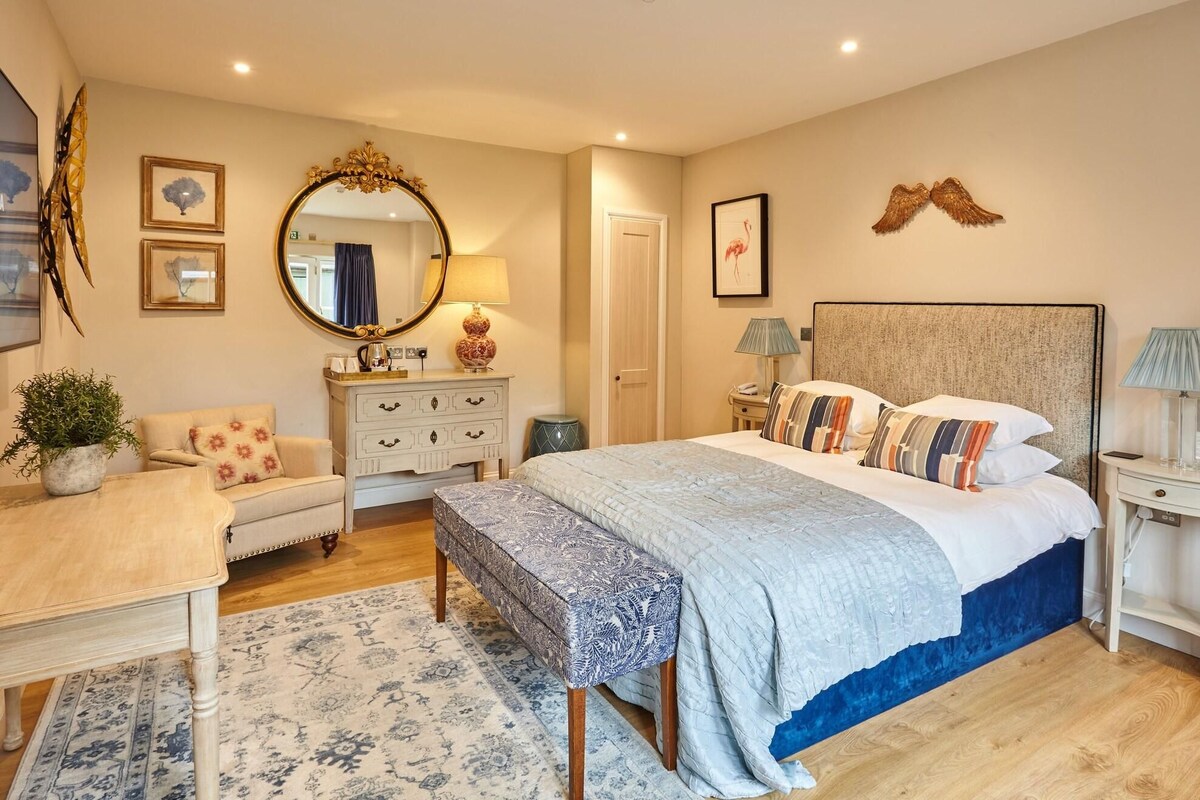 Un dormitorio con cama, mesitas de noche, cómoda, espejo y lámpara de pared.