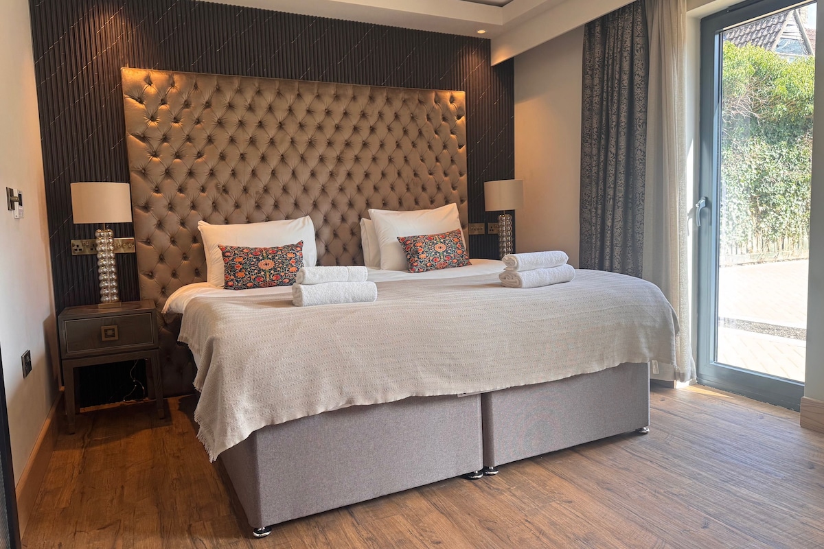 Habitación de hotel con una cama grande, cabecera, dos mesitas de noche y vistas al exterior.