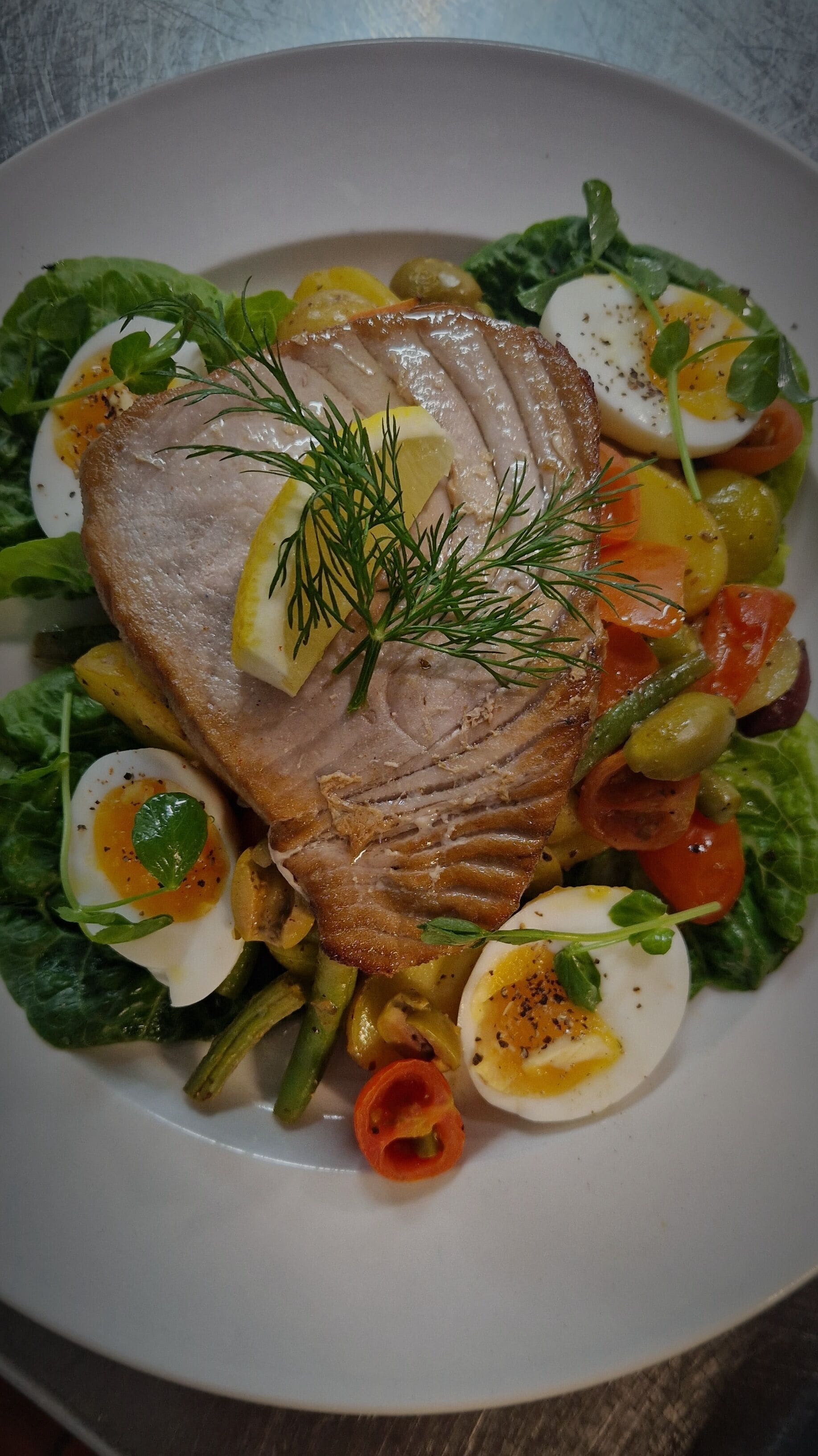 A plate of food with a slice of meat, boiled eggs, and vegetables.