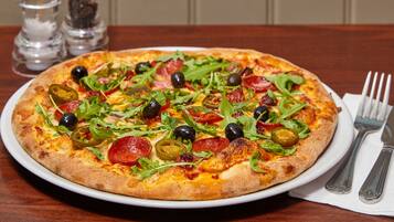 A pizza with various toppings on a white plate, placed on a wooden table with salt and pepper shakers in the background.