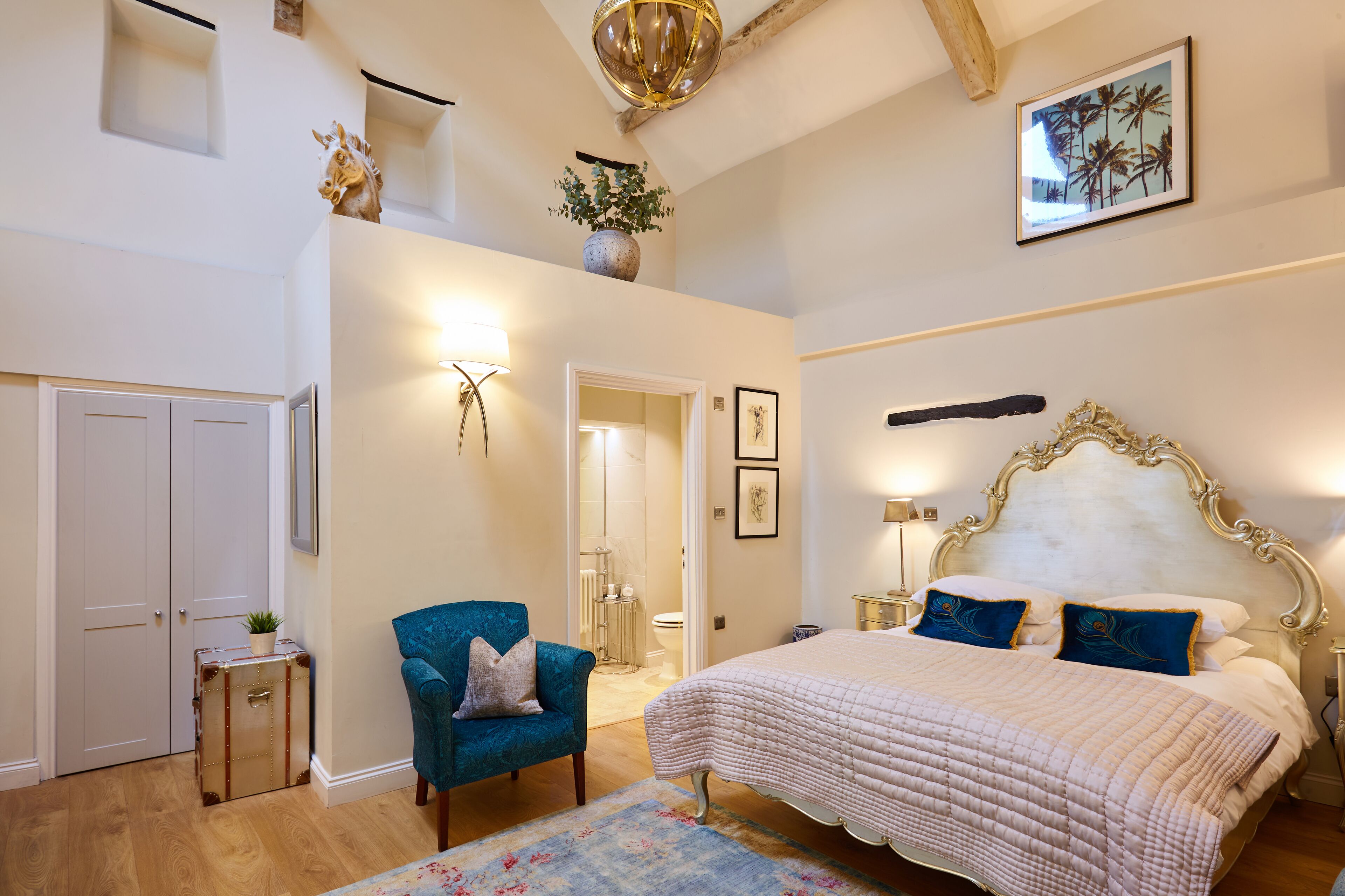 A bedroom with a large bed, a blue armchair, a chest of drawers, and a small table with a plant.