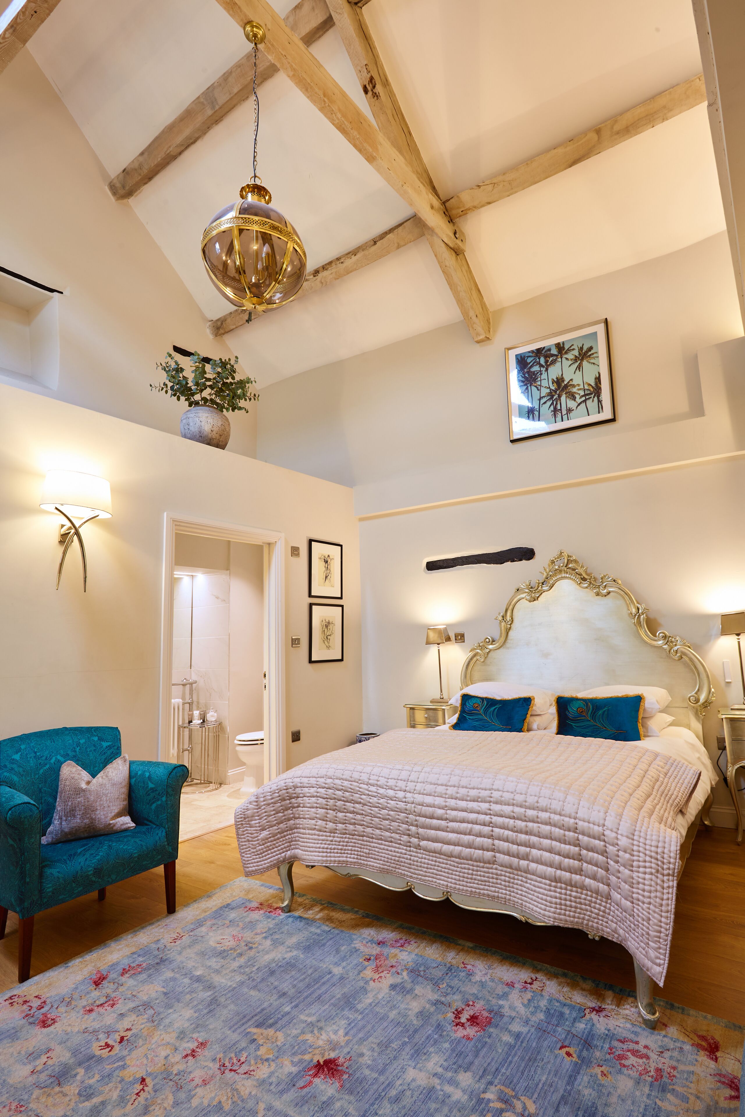 Un dormitorio con una cama grande, una araña, un sillón azul y un tapete floral.