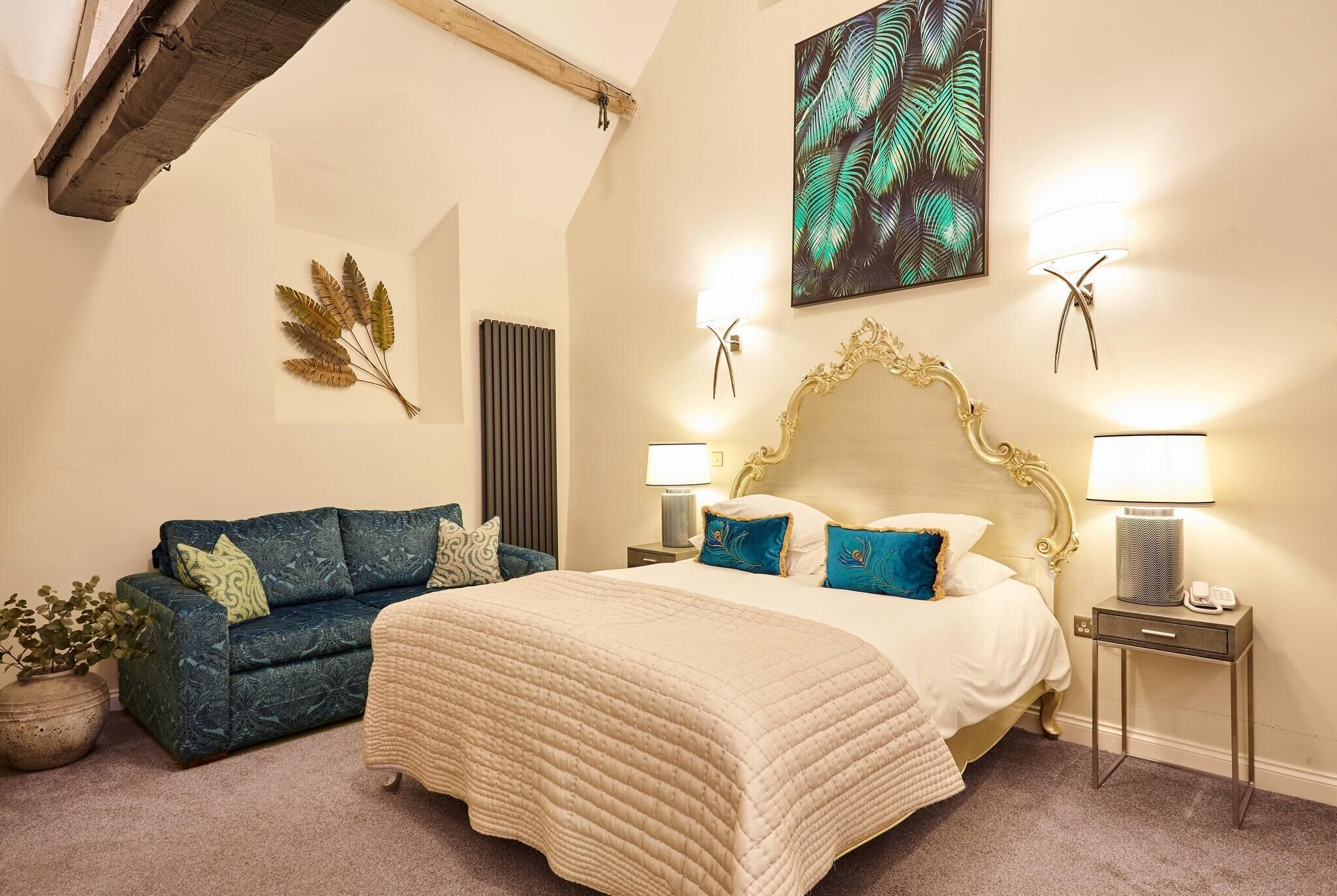 A bedroom with a bed, a blue sofa, decorative wall art, and bedside lamps.