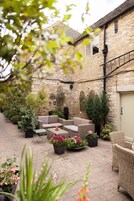 Un patio con muros de piedra, muebles de mimbre y plantas en macetas.