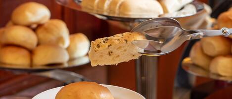 Un bufé con diversas opciones de panadería, como panes y bollos, presentados en soportes metálicos.