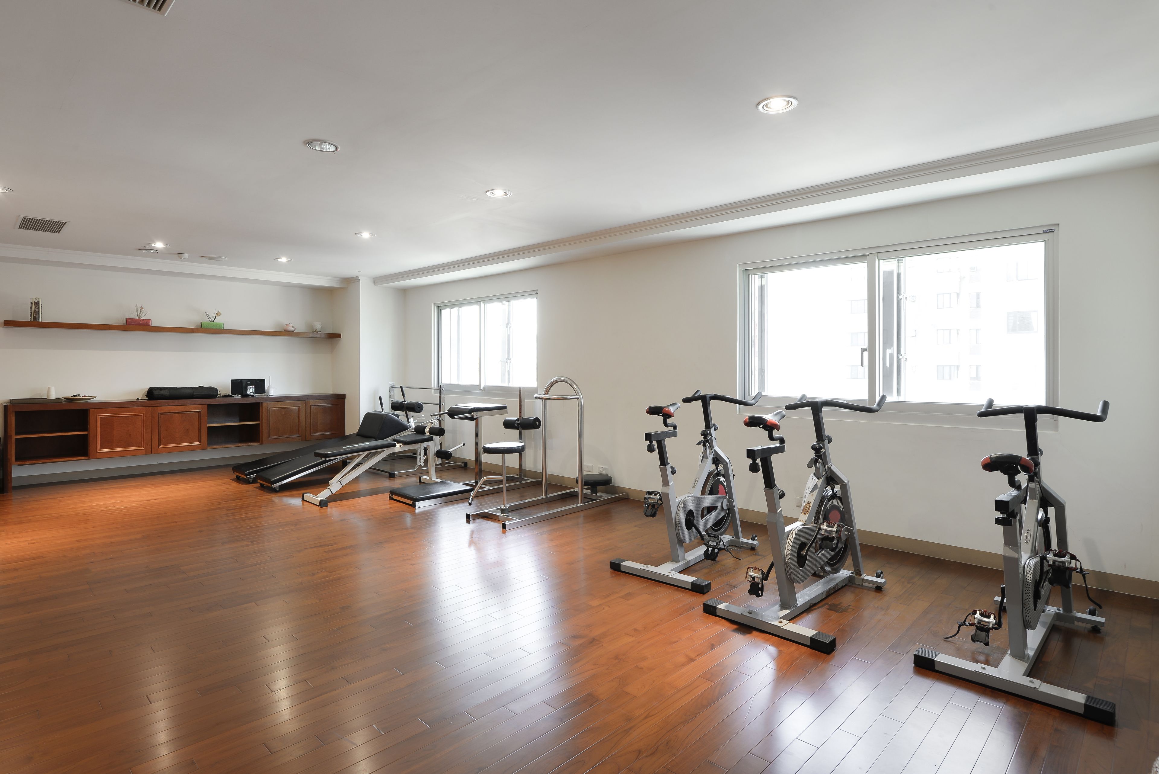 Une pièce spacieuse dotée d’un plancher en bois franc, d’un tapis de course, de vélos d’appartement et d’un banc de musculation.