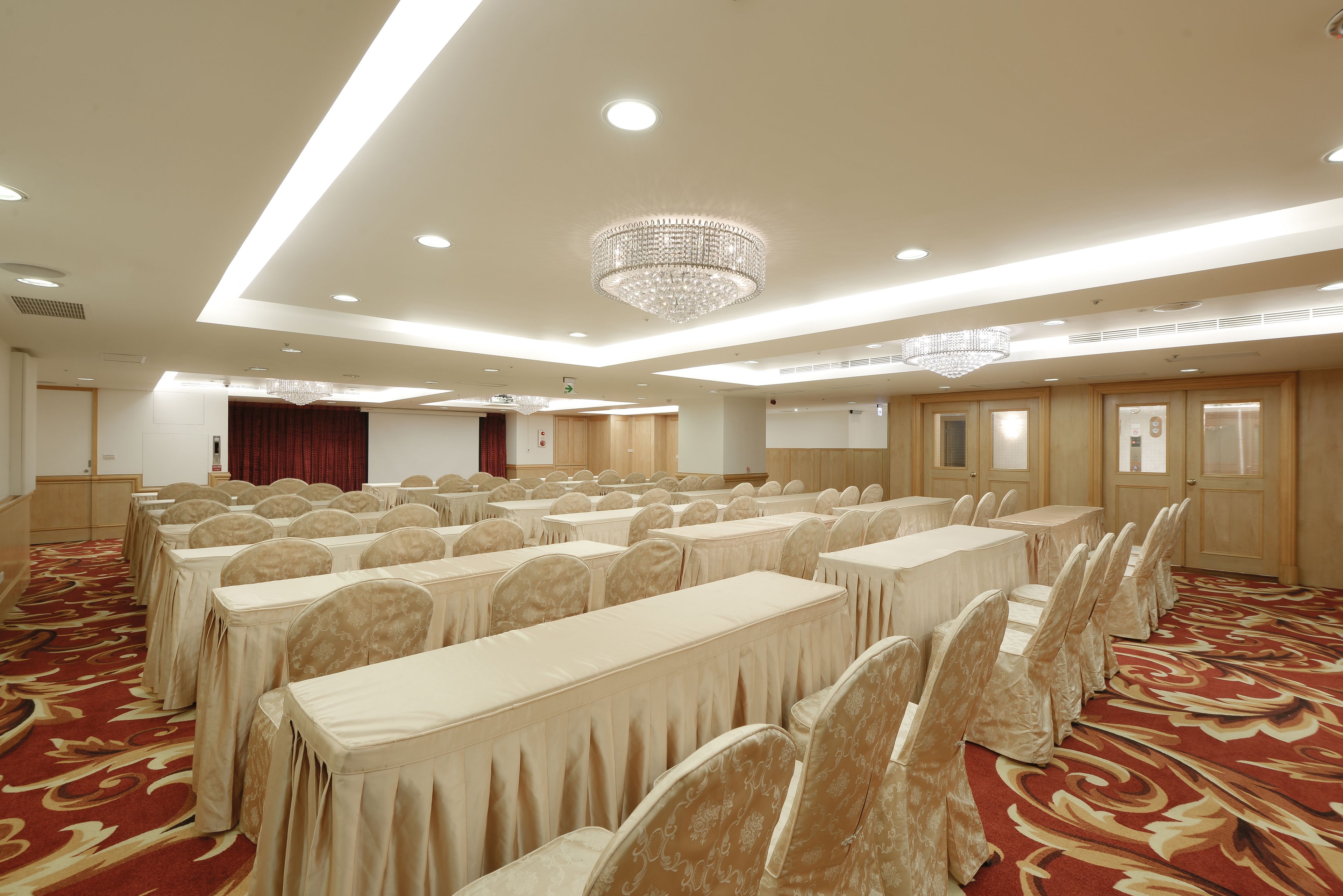 A conference room with rows of tables and chairs, a chandelier, and a red carpeted floor.